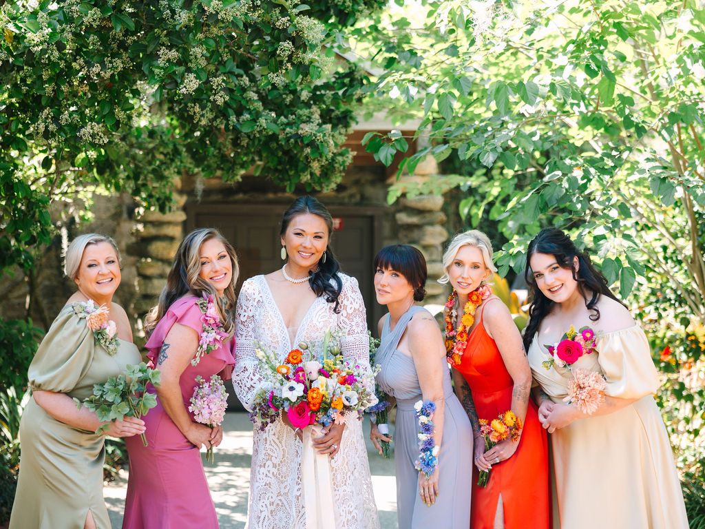 A group of beautiful women, holding flowers, are smiling radiantly in the sunlight.