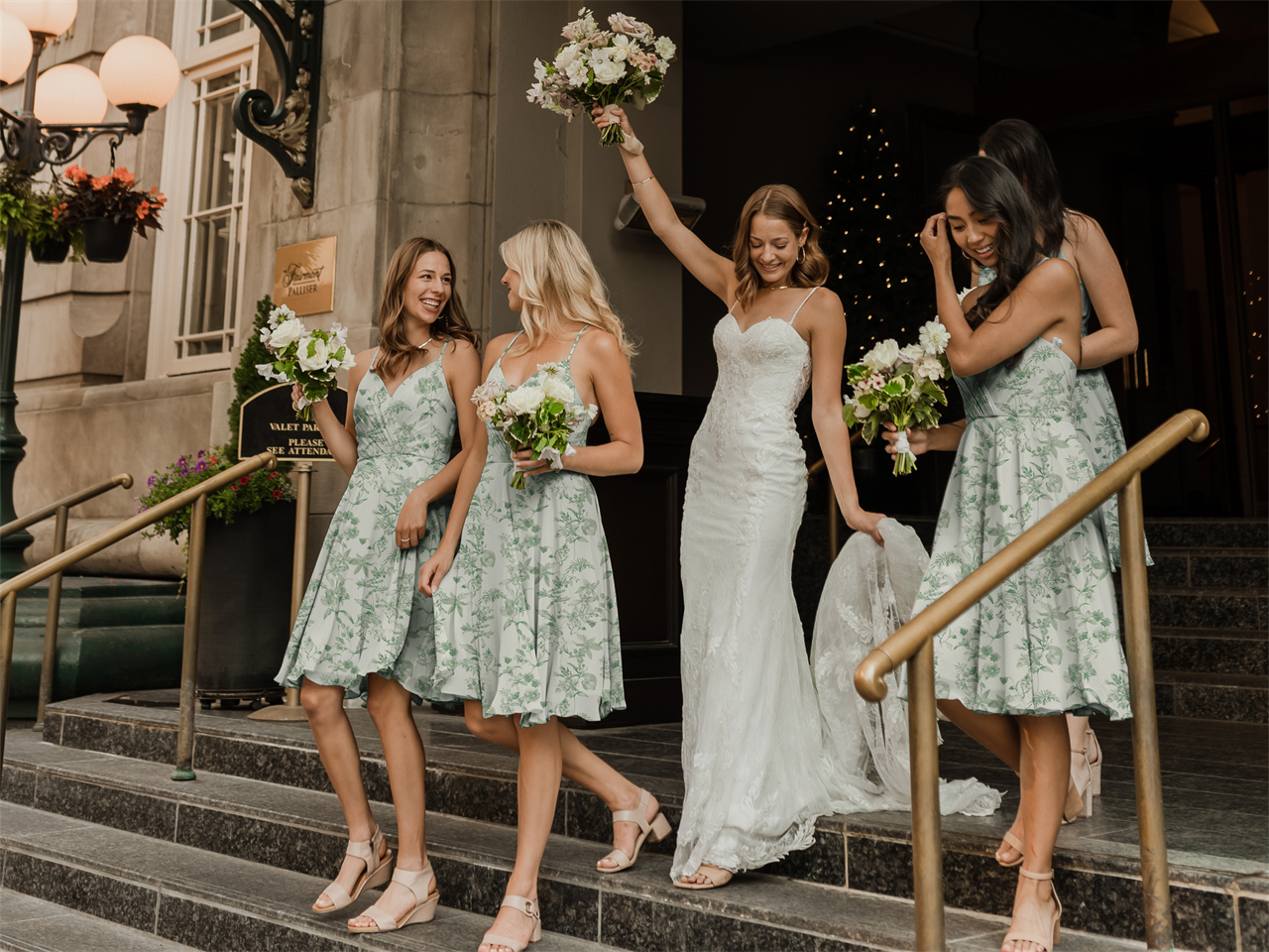 Bride flanked by bridesmaids in green floral dresses, all holding bouquets and smiling