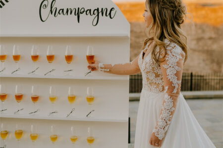 A bride standing next to rows of champagne flutes, holding one in her hand.