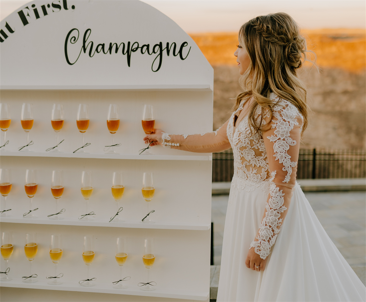 A bride standing next to rows of champagne flutes, holding one in her hand.