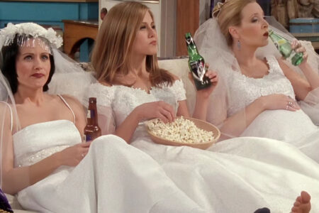 Monica, Rachel, and Phoebe from "Friends" sitting on a couch in wedding dresses.